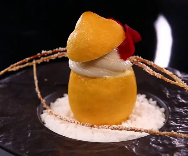 Dessert raffiné au citron composé d’un sorbet, surmonté d’une crème, avec une décoration sucrée incluant une pétale de rose et une présentation élégante.
