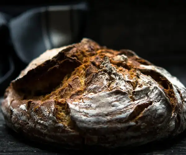 Découvrez notre boule de pain de campagne rustique avec une croûte bien dorée, une saveur craquante et farinée, présentée sur un fond sombre pour mettre en valeur sa texture artisanale, fabriquée par notre boulanger de la Table de 3 à Bordeaux.